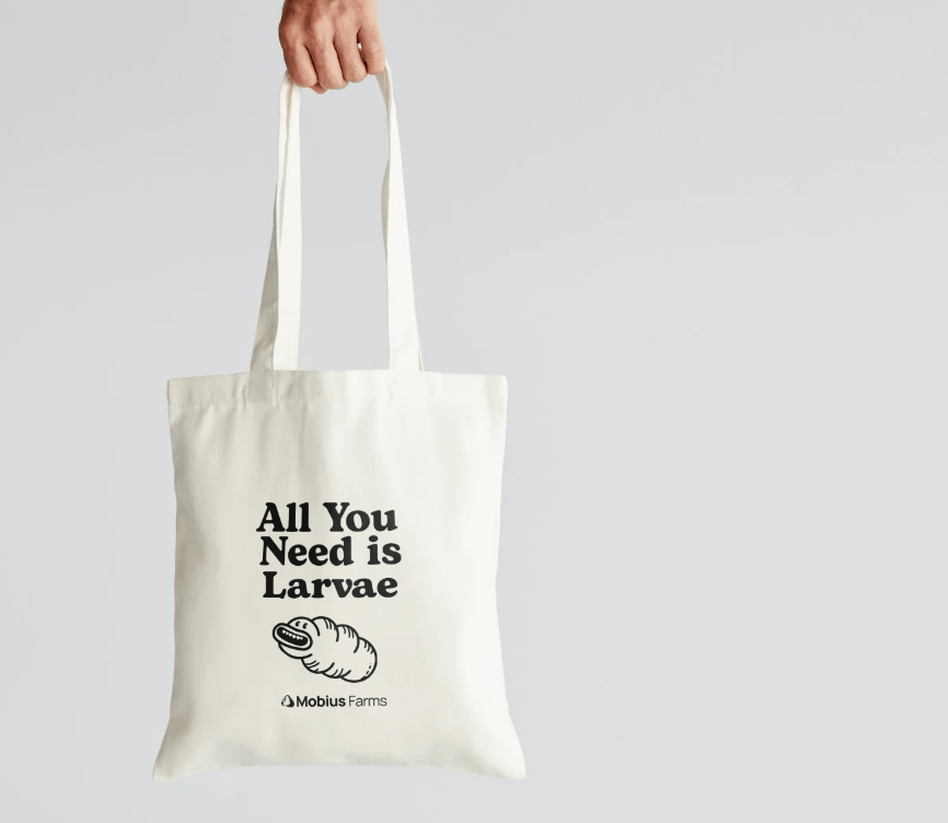 Tote bag with 'All You Need is Larvae' text and Mobius Farms logo on a light gray background