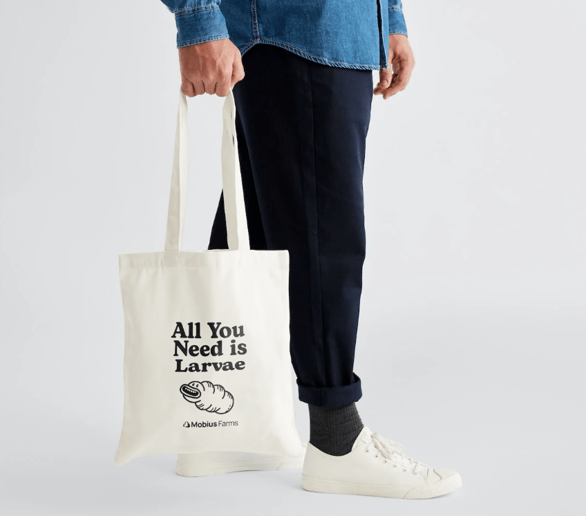 Person holding a tote bag with text and logo on a light gray background